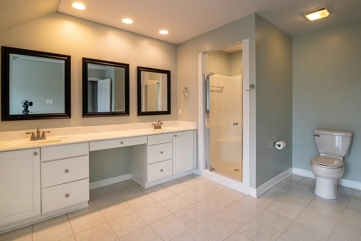 Primary bathroom with long vanity, double mirrors, tile floor, toilet, and glass shower