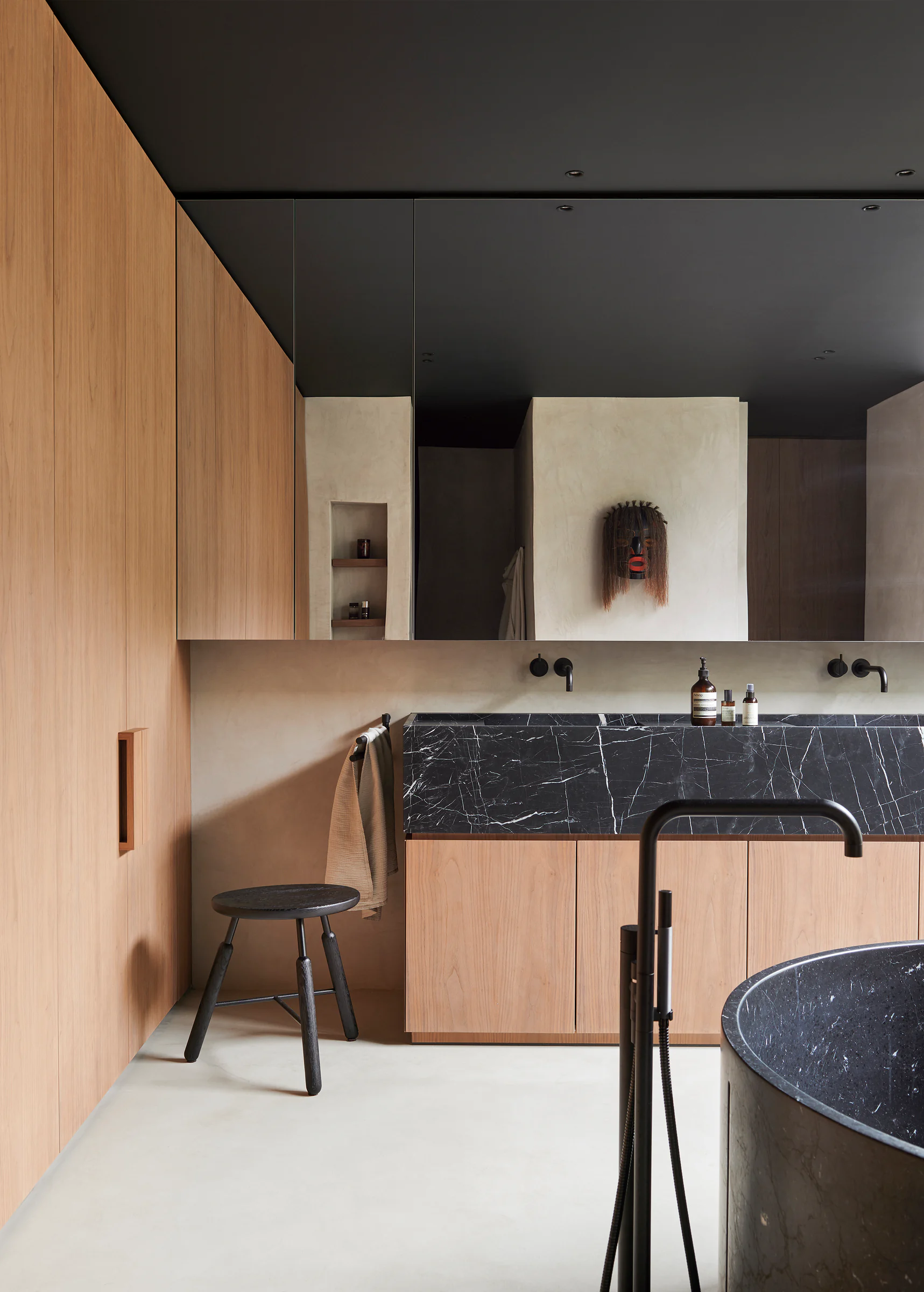 Bathroom vanity with pale wood storage, black stone counter, mirror wall, and precise finish lines